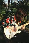 A person in a floral shirt plays guitar with their long hair obstructing their face.
