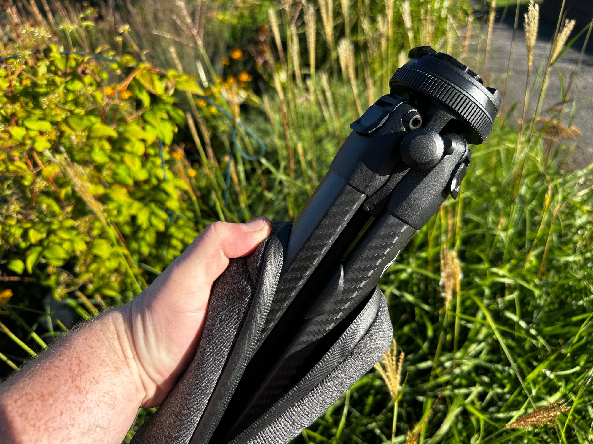 A hand holds the Peak Design Travel Tripod against green foliage.